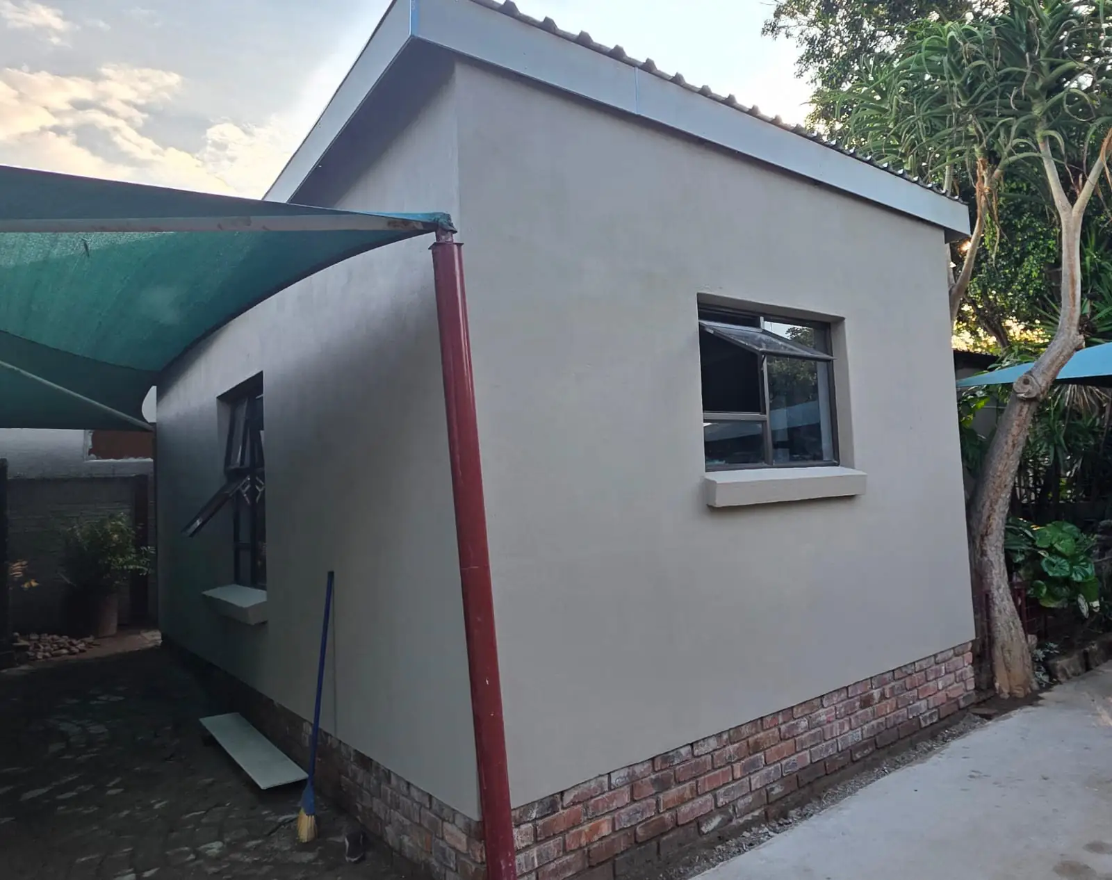A newly built outbuilding with smooth plastered walls on a face-brick plinth, a charcoal aluminium window and a boxed roof edge.