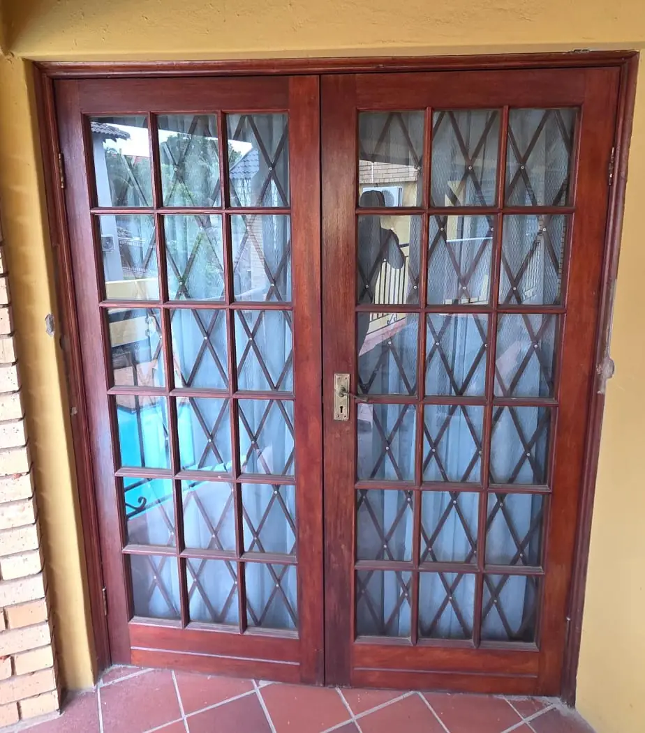 Old mahogany French doors divided into small panes and backed with diamond security mesh, opening off a terracotta-tiled floor.